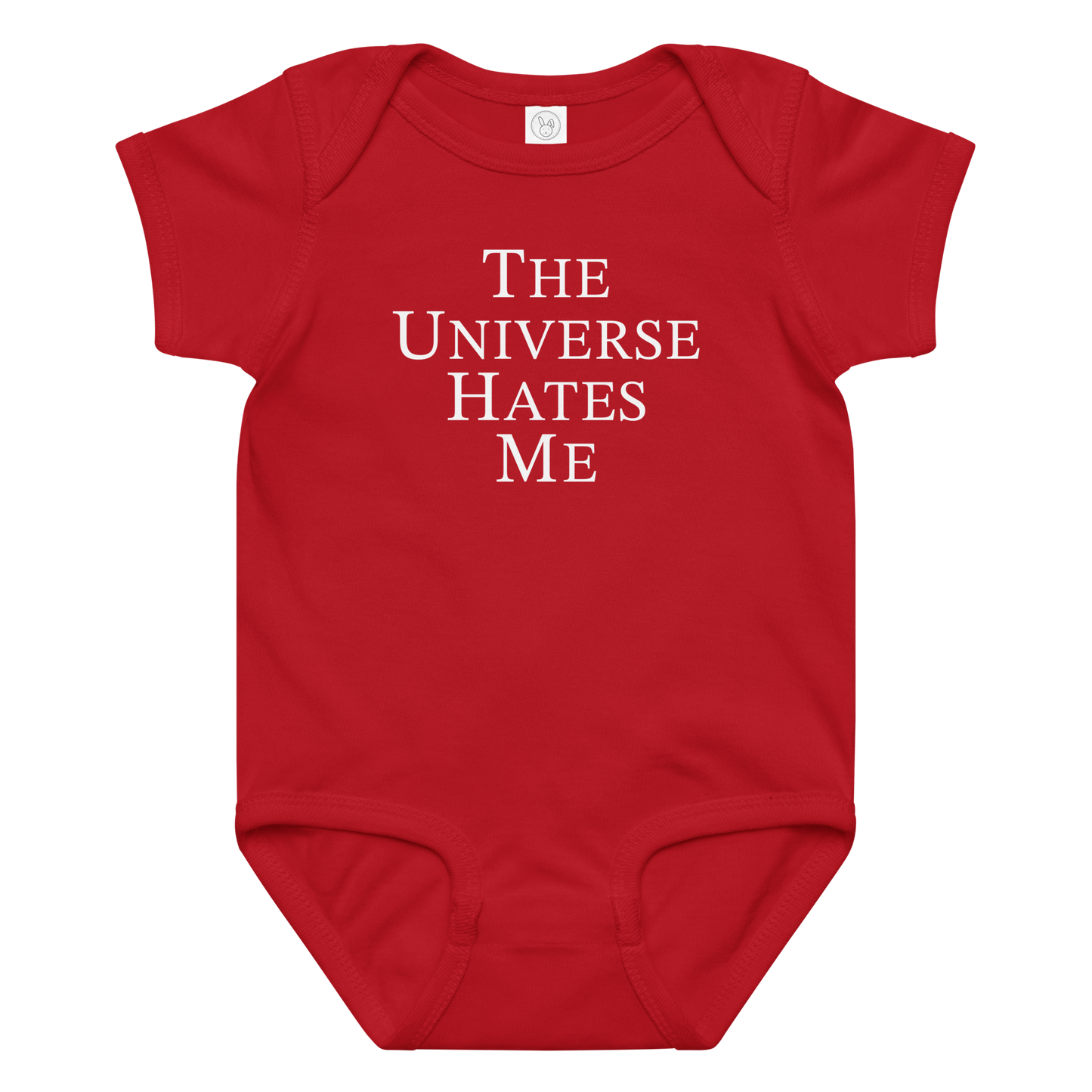 "The Universe Hates Me" printed on a red baby jersey bodysuit laying on a flat surface amongst other clothes