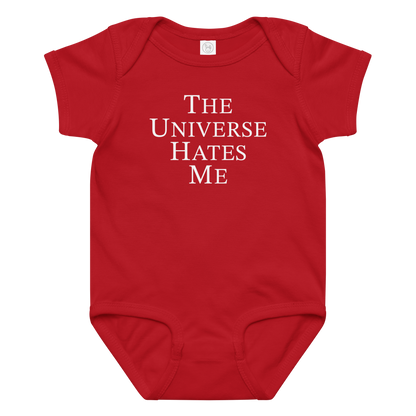 "The Universe Hates Me" printed on a red baby jersey bodysuit laying on a flat surface amongst other clothes