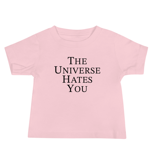 "The Universe Hates You" printed on a pink baby jersey short sleeve tee laying on a flat surface
