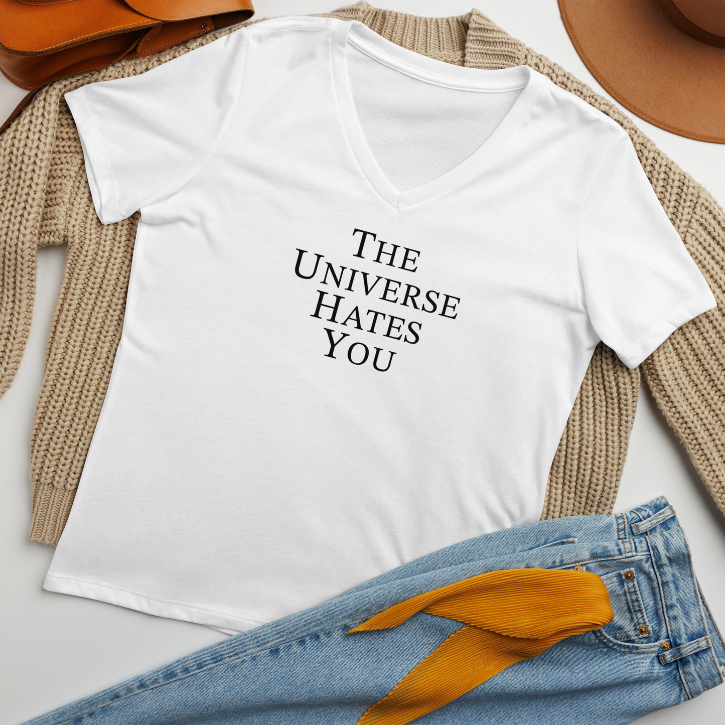 "The Universe Hates You" printed on a solid white blend women's relaxed v-neck t-shirt laying on a flat surface amongst other clothes