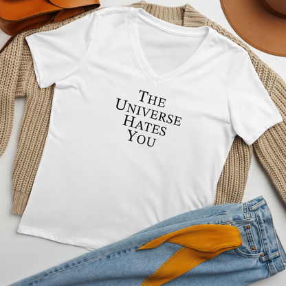 "The Universe Hates You" printed on a solid white blend women's relaxed v-neck t-shirt laying on a flat surface amongst other clothes
