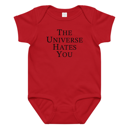 "The Universe Hates You" printed on a red baby jersey bodysuit laying on a flat surface amongst other clothes