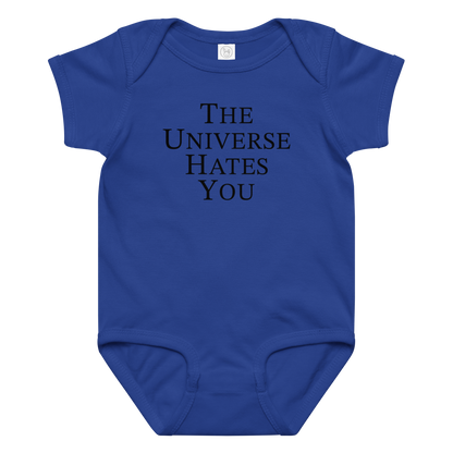"The Universe Hates You" printed on a royal baby jersey bodysuit laying on a flat surface amongst other clothes