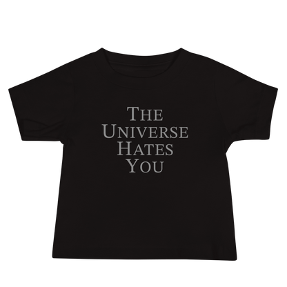 "The Universe Hates You" printed on a black baby jersey short sleeve tee laying on a flat surface