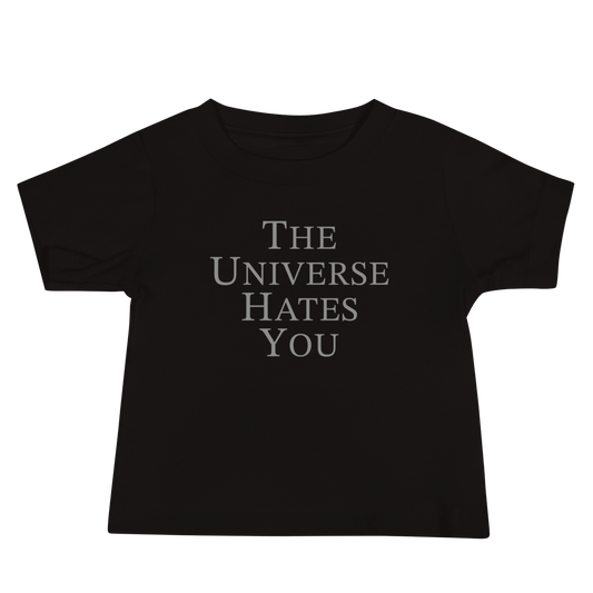 "The Universe Hates You" printed on a black baby jersey short sleeve tee laying on a flat surface