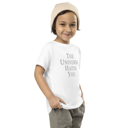 "The Universe Hates You" printed on a white toddler short sleeve tee worn by a male who is also wearing a knit cap