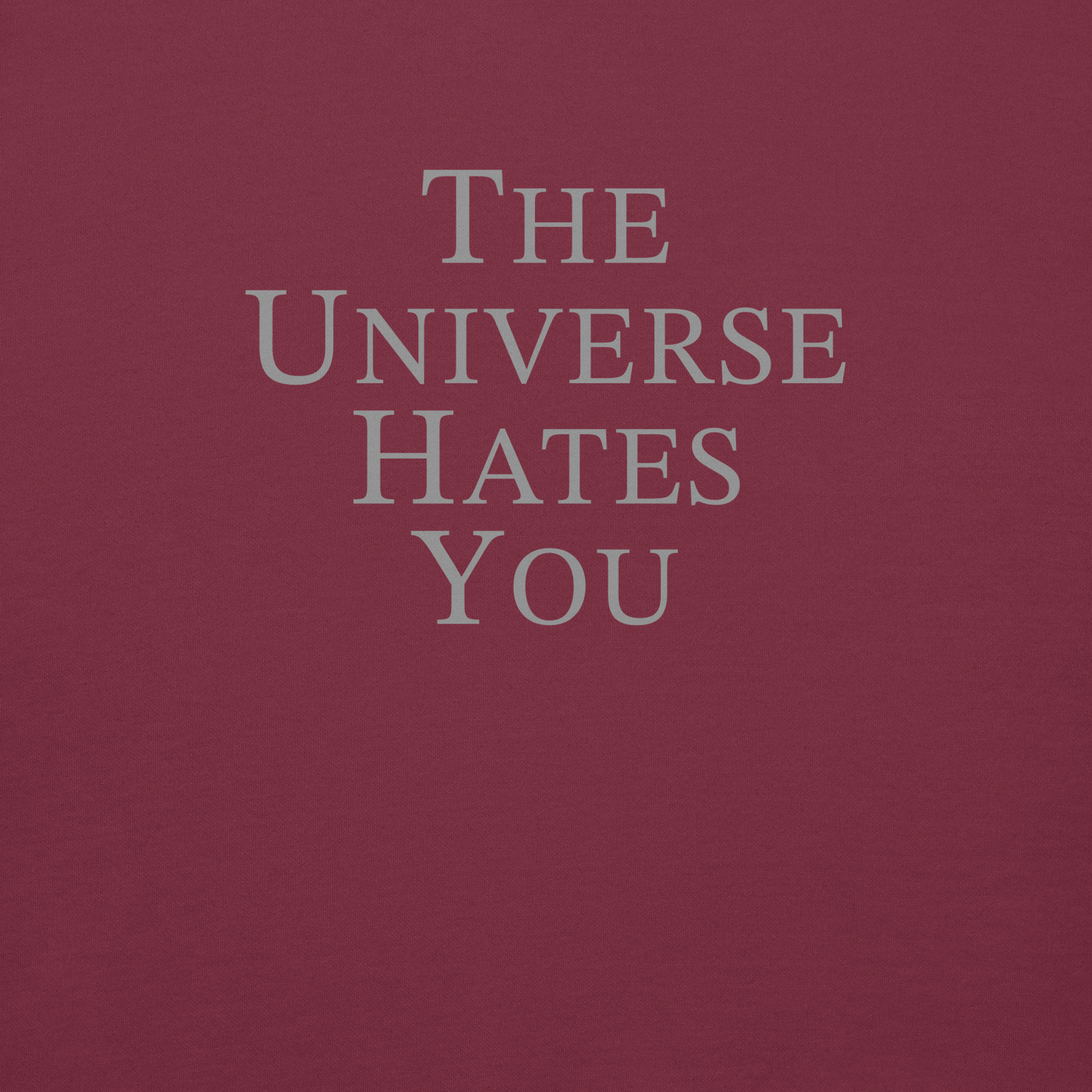 "The Universe Hates You" printed on a maroon background