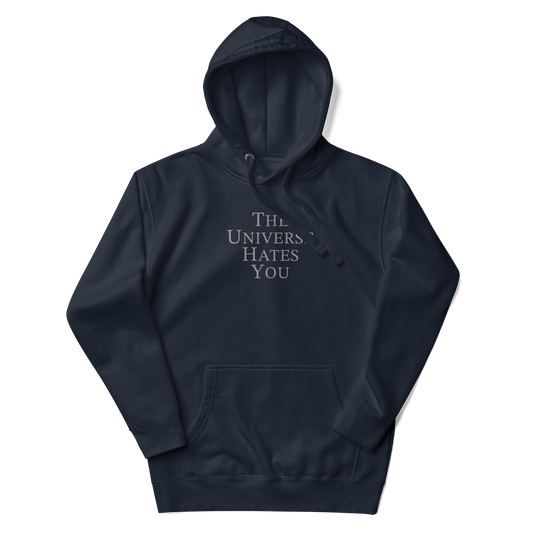 "The Universe Hates You" printed on a navy blazer unisex hoodie laying on a flat surface with the hood up