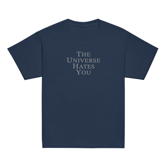 "The Universe Hates You" printed on a navy youth classic tee laying on a flat surface