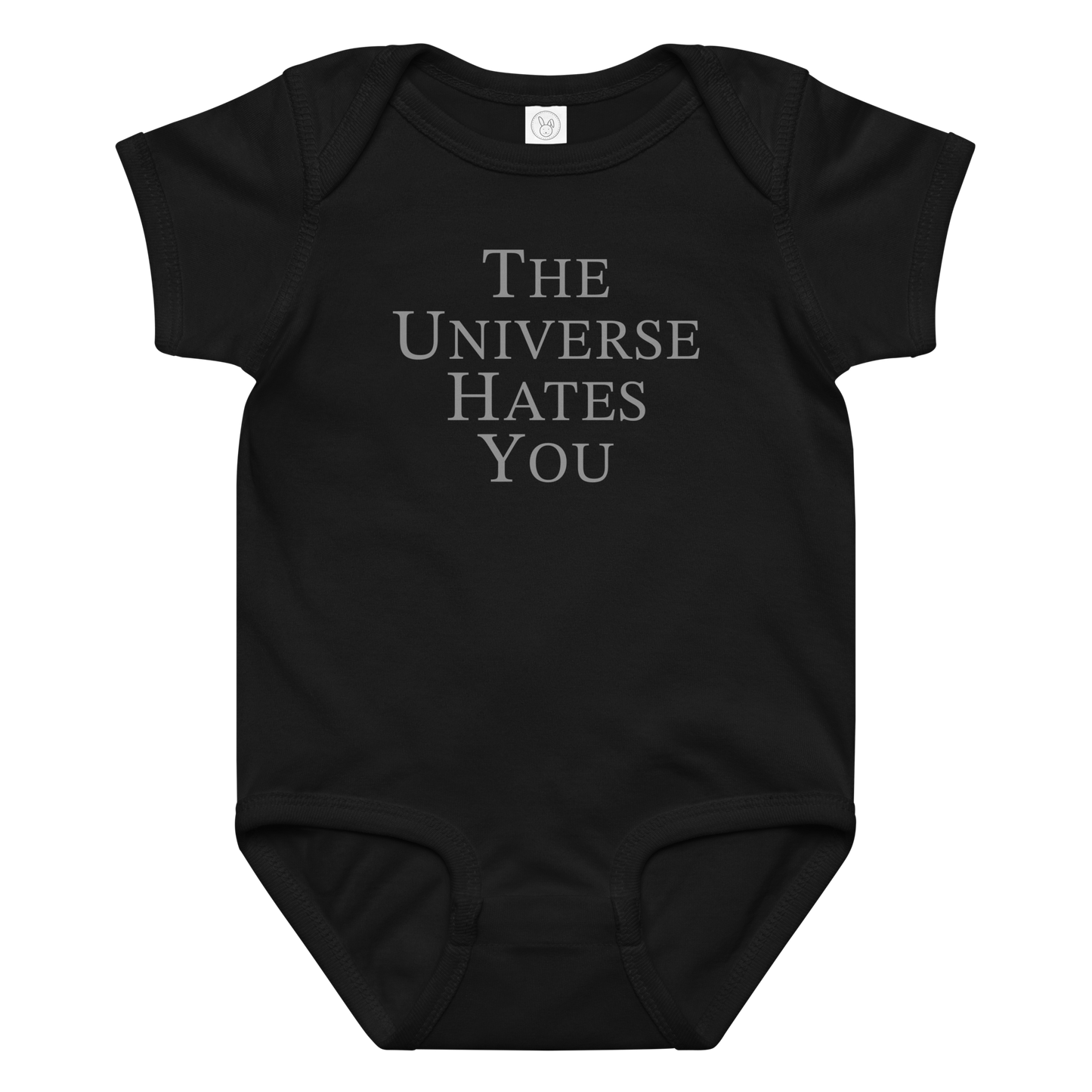 "The Universe Hates You" printed on a black baby jersey bodysuit laying on a flat surface amongst other clothes