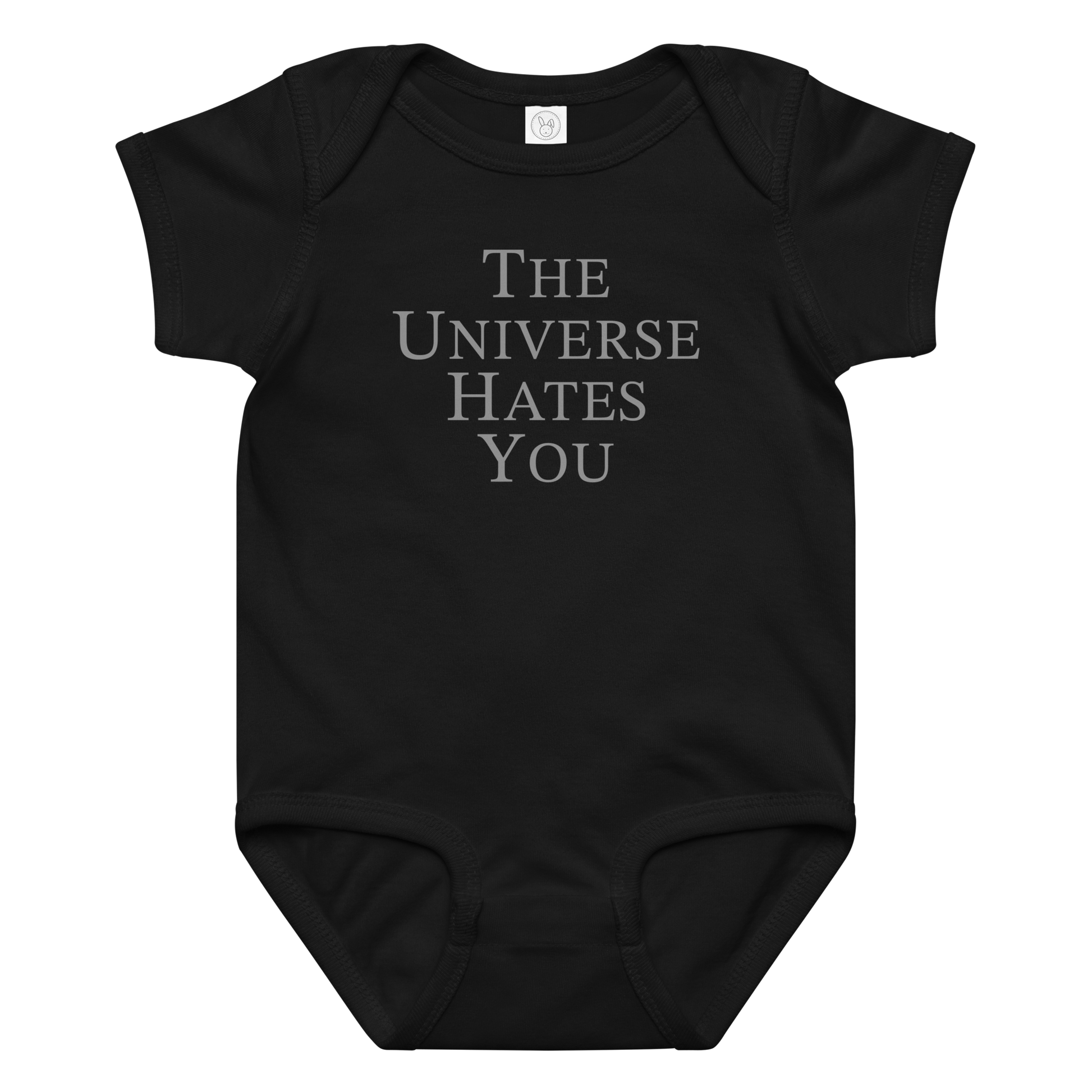 "The Universe Hates You" printed on a black baby jersey bodysuit laying on a flat surface amongst other clothes