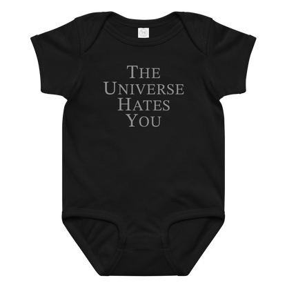 "The Universe Hates You" printed on a black baby jersey bodysuit laying on a flat surface amongst other clothes