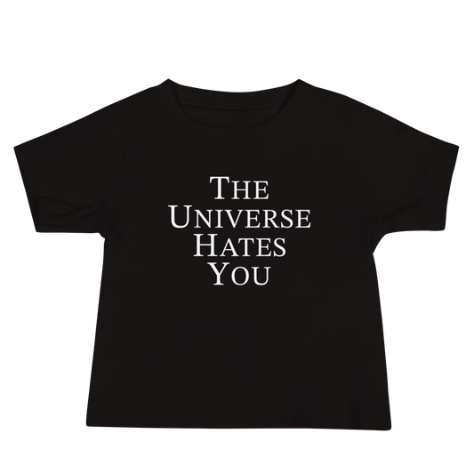"The Universe Hates You" printed on a black baby jersey short sleeve tee laying on a flat surface