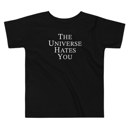 "The Universe Hates You" printed on a black toddler short sleeve tee laying on a flat surface