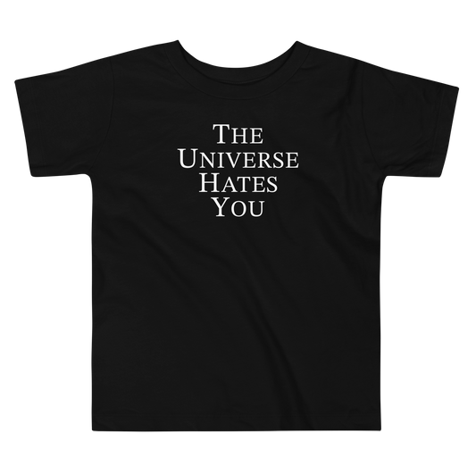 "The Universe Hates You" printed on a black toddler short sleeve tee laying on a flat surface