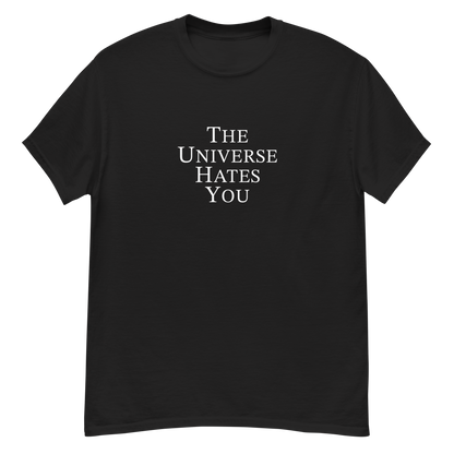 "The Universe Hates You" printed on a black unisex classic tee laying on a flat surface
