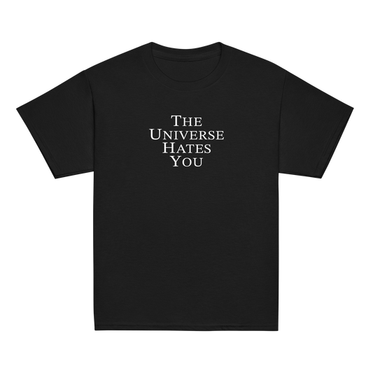 "The Universe Hates You" printed on a black youth classic tee laying on a flat surface