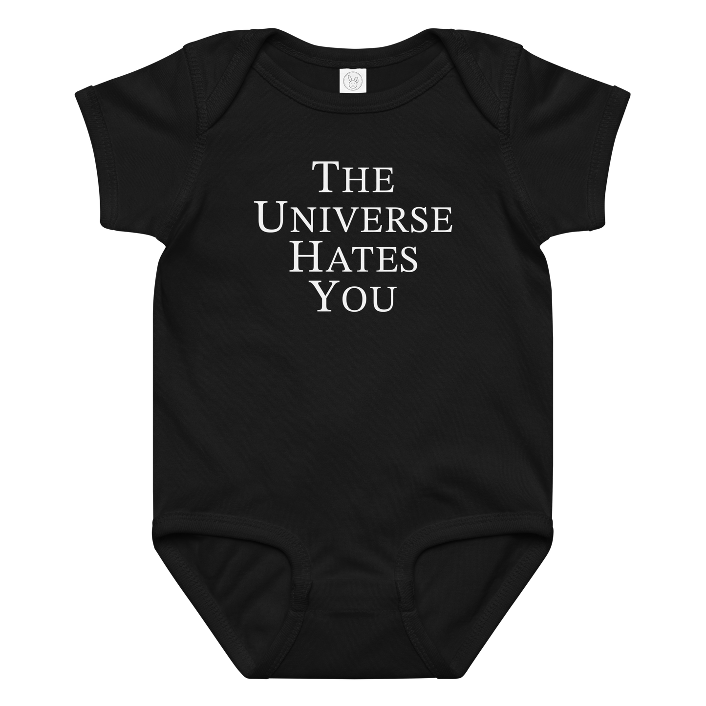 "The Universe Hates You" printed on a black baby jersey bodysuit laying on a flat surface amongst other clothes