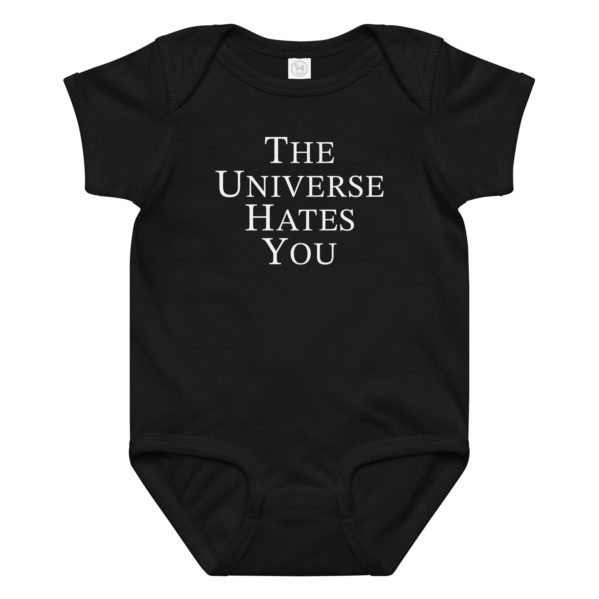 "The Universe Hates You" printed on a black baby jersey bodysuit laying on a flat surface amongst other clothes