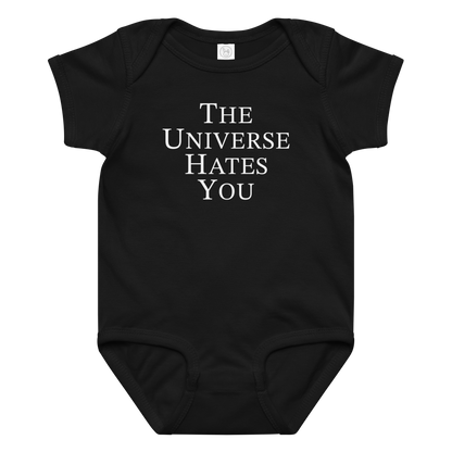 "The Universe Hates You" printed on a black baby jersey bodysuit laying on a flat surface amongst other clothes