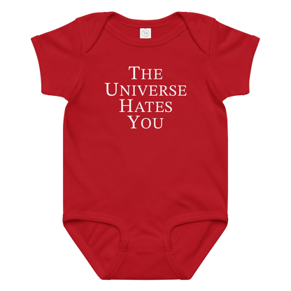 "The Universe Hates You" printed on a red baby jersey bodysuit laying on a flat surface amongst other clothes
