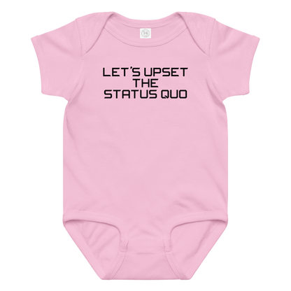 "Let's upset the status quo!" printed on a pink baby jersey bodysuit laying on a flat surface amongst other clothes