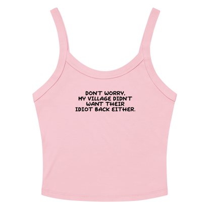 "Don't worry, my village didn’t want their idiot back either." printed on a solid pink blend women's micro-rib tanktop laying on a flat surface amongst sunglasses and shorts