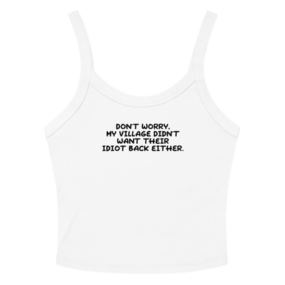 "Don't worry, my village didn’t want their idiot back either." printed on a solid white blend women's micro-rib tanktop laying on a flat surface amongst sunglasses and shorts