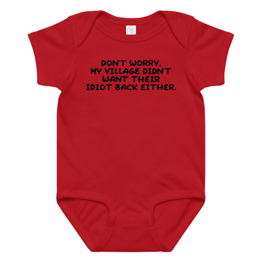 "Don't worry, my village didn’t want their idiot back either." printed on a red baby jersey bodysuit laying on a flat surface amongst other clothes