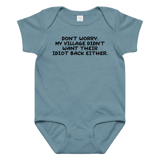"Don't worry, my village didn’t want their idiot back either." printed on a vintage indigo baby jersey bodysuit laying on a flat surface amongst other clothes