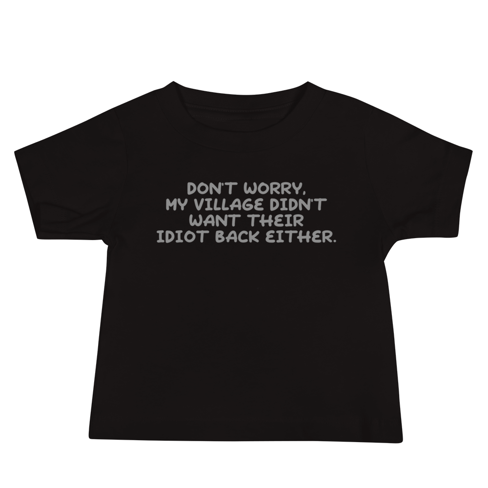 "Don't worry, my village didn’t want their idiot back either." printed on a black baby jersey short sleeve tee laying on a flat surface