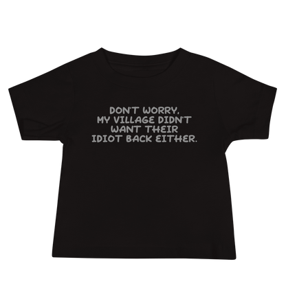 "Don't worry, my village didn’t want their idiot back either." printed on a black baby jersey short sleeve tee laying on a flat surface