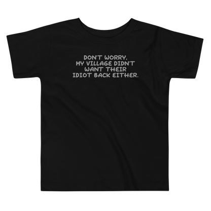 "Don't worry, my village didn’t want their idiot back either." printed on a black toddler short sleeve tee laying on a flat surface