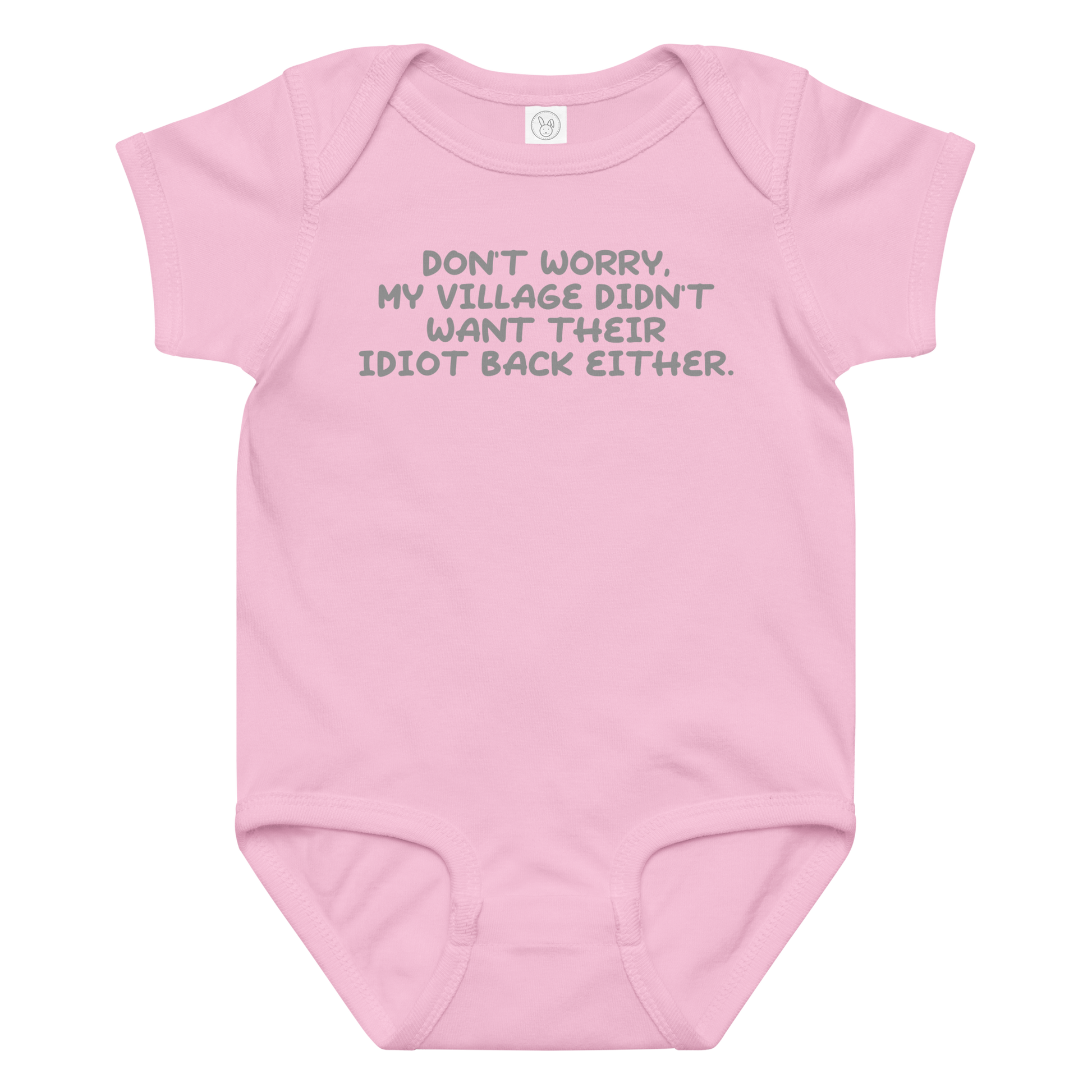 "Don't worry, my village didn’t want their idiot back either." printed on a pink baby jersey bodysuit laying on a flat surface amongst other clothes