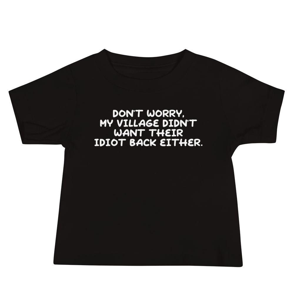"Don't worry, my village didn’t want their idiot back either." printed on a black baby jersey short sleeve tee laying on a flat surface