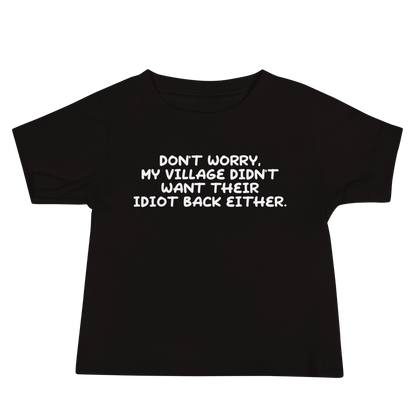"Don't worry, my village didn’t want their idiot back either." printed on a black baby jersey short sleeve tee laying on a flat surface
