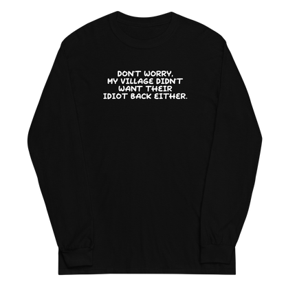 "Don't worry, my village didn’t want their idiot back either." printed on a black men's long sleeve shirt laying on a flat surface