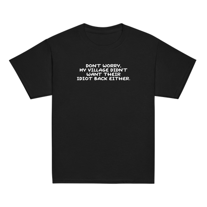 "Don't worry, my village didn’t want their idiot back either." printed on a black youth classic tee laying on a flat surface