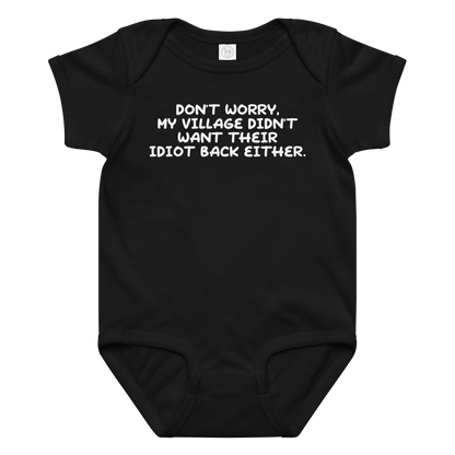 "Don't worry, my village didn’t want their idiot back either." printed on a black baby jersey bodysuit laying on a flat surface amongst other clothes