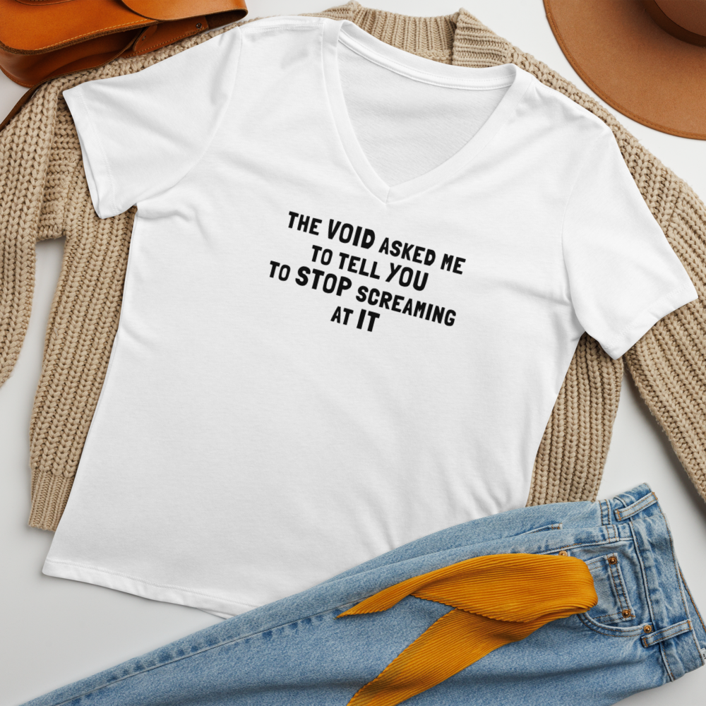 "The Void asked me to tell you to stop screaming at it" printed on a solid white blend women's relaxed v-neck t-shirt laying on a flat surface amongst other clothes