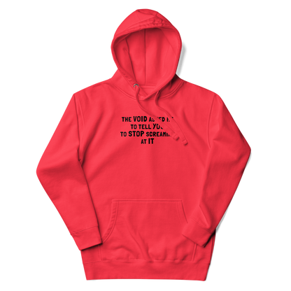 "The Void asked me to tell you to stop screaming at it" printed on a team red unisex hoodie laying on a flat surface with the hood up