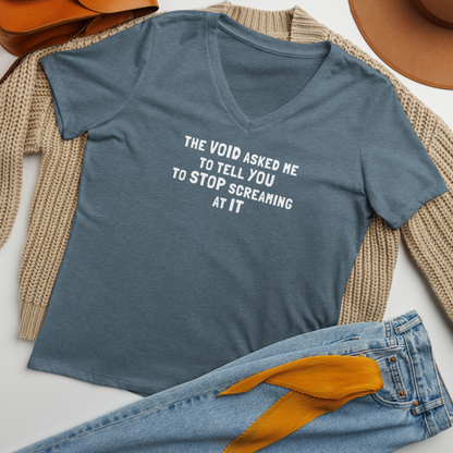 "The Void asked me to tell you to stop screaming at it" printed on a heather slate women's relaxed v-neck t-shirt laying on a flat surface amongst other clothes
