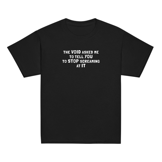 "The Void asked me to tell you to stop screaming at it" printed on a black youth classic tee laying on a flat surface