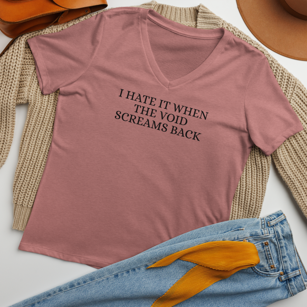 "I hate it when the void screams back" printed on a heather mauve women's relaxed v-neck t-shirt laying on a flat surface amongst other clothes