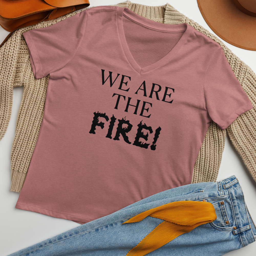 "We are the fire!" printed on a heather mauve women's relaxed v-neck t-shirt laying on a flat surface amongst other clothes