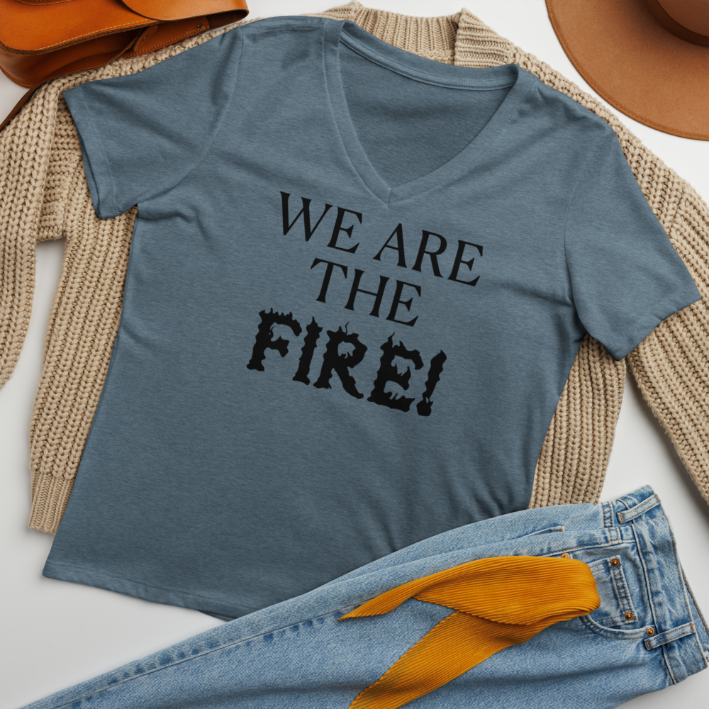 "We are the fire!" printed on a heather slate women's relaxed v-neck t-shirt laying on a flat surface amongst other clothes