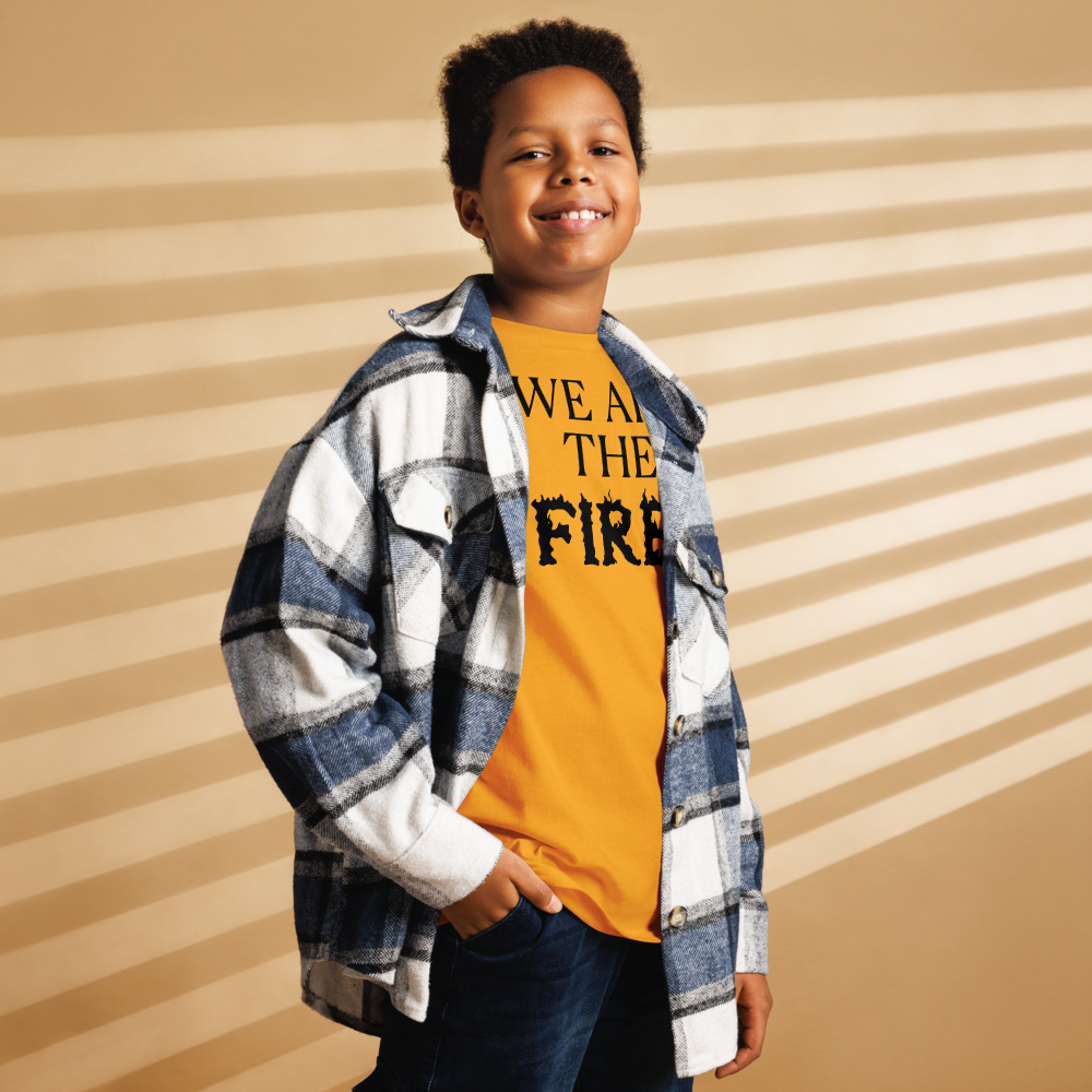 "We are the fire!" printed on a gold youth classic tee worn by a male also wearing a jacket