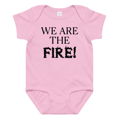"We are the fire!" printed on a pink baby jersey bodysuit laying on a flat surface amongst other clothes