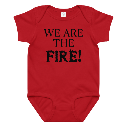 "We are the fire!" printed on a red baby jersey bodysuit laying on a flat surface amongst other clothes