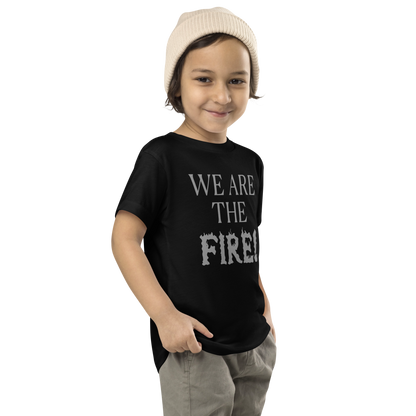 "We are the fire!" printed on a black toddler short sleeve tee worn by a male who is also wearing a knit cap